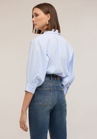 Camicia a righe blu con vestibilità morbida e maniche arrotolate, abbinata a jeans blu scuro a vita alta con tasche posteriori.