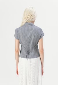 Kortermet, figursydd skjorte i marineblått og hvitt gingham-mønster, med krage og knyting bak i livet.