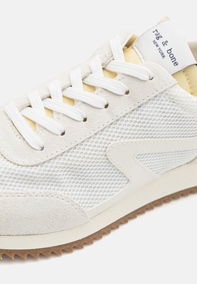 White sneaker with a mesh upper, suede accents, flat white laces, and a textured rubber sole. Features light yellow lining and a logo tag.