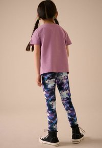 T-shirt en coton violet et leggings ajustés ornés d'un imprimé abstrait multicolore. Des baskets montantes noires complètent la tenue.