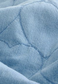 Svetlo modra prešita tkanina z teksturirano površino in ukrivljenimi šivi, ki vključuje mehak denim podoben material.