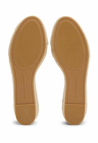 Suole in gomma di un beige chiaro con superficie testurizzata e leggera curvatura. Logo impresso nell'area del tallone. Design semplice e minimalista.