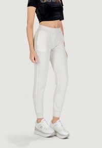 Pantaloni jogger bianchi con una texture liscia e una fascia elastica in vita, dotati di tasche laterali e polsini a costine, abbinati a sneaker bianche.