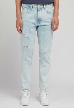 Jasnoniebieskie spodnie dżinsowe z efektem przetarcia, z charakterystycznymi dziurami, wysoki stan, proste nogawki. W połączeniu z białymi trampkami i teksturowanymi skarpetkami.