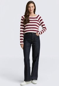 Punase ja valge triibuline pika varrukaga pluus koos kõrge vöökohaga tumedate laienevate teksapükstega. Modell kannab valgeid tossusid, käed taskutes.