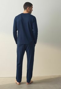 Marineblauw longsleeve shirt en bijpassende broek van zacht materiaal, met een eenvoudig ontwerp en een ontspannen pasvorm. Geen zichtbare patronen of accenten.