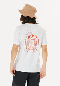 Vit kortärmad t-shirt med en orange grafik av en skåpbil, berg, sol och träd på baksidan. Materialet verkar lätt och mjukt.