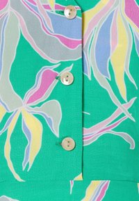 Green fabric featuring large floral patterns in pink, yellow, and blue, with three buttons made of a light-colored material.