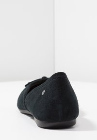 Černá semišová plochá bota s kulatou zadní částí, obsahující malý akcentní detail blízko paty a hladkou černou gumovou podrážku.