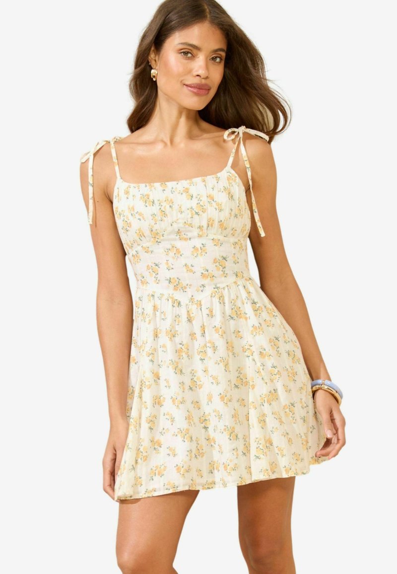 Rochie de soare florală în galben deschis, cu modele mici de flori, decolteu pătrat, bretele ajustabile și fustă fluidă. Textură de material neted.