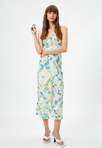 Halter-neck midi klänning i vitt med blå och gröna tie-dye mönster, med samlade detaljer och en slits framtill, matchad med vita klackar.