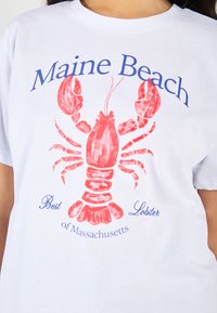 Hvid t-shirt med et stort rødt hummergrafik og blå tekst, der siger "Maine Beach" og "Best Lobster of Massachusetts."