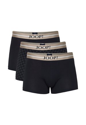 Stehender, oberkörperfreier Mann, der schwarze Boxershorts mit einem grauen Bund trägt, auf dem "JOOP!" steht, vor einem einfarbigen hellen Hintergrund.