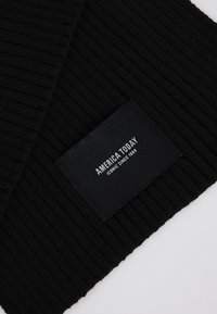 Gorro negro de canalé con una etiqueta tejida que muestra "AMERICA TODAY" y "ICONIC SINCE 1989". Textura suave, diseño casual y ajuste ceñido.