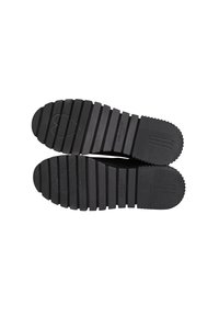 Suole di scarpe in gomma nera con scanalature profonde, caratterizzate da motivi orizzontali e verticali, e un logo a forma di cuore impresso su una suola.