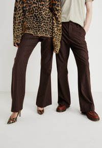 Leopard print knit sweater, brown pinstripe trousers, and assorted footwear: heeled leopard print shoes and brown lace-up shoes.