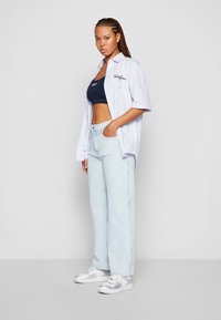 Maglietta a maniche corte a righe blu chiaro sopra un top navy accorciato, con jeans larghi blu chiaro e sneaker argentate.