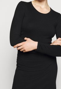 Haut noir à manches longues avec un design ajusté, texture côtelée et col rond. Le tissu semble doux et extensible.