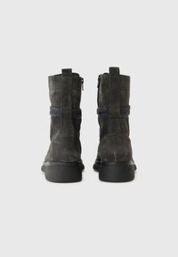Stivali ankle in suede nera con una fascia grigia texture, suola in gomma piatta e chiusura con zip laterale, dotati di tacco rinforzato e linguetta per estrazione.