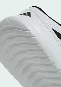 Gros plan de la semelle blanche d'une chaussure de sport avec des rainures texturées courbes et un logo noir sur la tige en mesh.