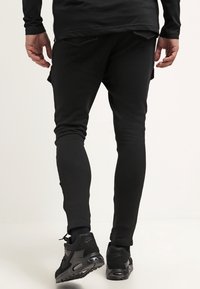 Svarta träningsbyxor med en figursydd design, tillverkade av stretcht material. Funktioner inkluderar sidofickor och de är kombinerade med svarta sneakers.