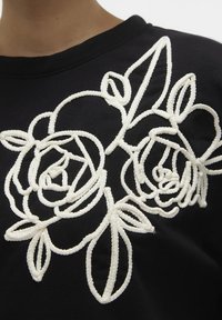 Sudadera negra con bordado en cordón blanco de rosas y hojas, con un acabado texturizado y detalles de costuras visibles.