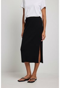 Sort ribbet midi-nederdel med en sideslids, der har en elastisk talje. Sammen med en hvid løstsiddende t-shirt og flade sandaler.