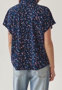 Korte mouw navy blouse met een bloemmotief in roze en blauw, met een kraag en een comfortabele pasvorm, gedragen met licht gewassen jeans.