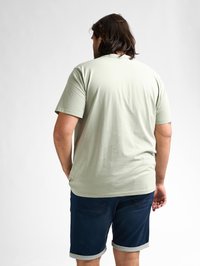 Lichtgroene t-shirt met korte mouwen en een ronde hals, gecombineerd met donkerblauwe denim shorts met opgekrulde zomen en achterzakken.
