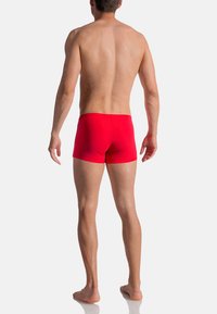 Röda simshorts med en tight passform och slät yta, med en enkel design. Bärs av en person som vänder ryggen mot kameran.