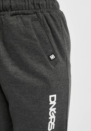 Pelēki treniņbikses ar strukturētu audumu, elastīgu jostasvietu, sānu kabatām un baltu logo uz kreisās kājas.