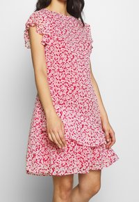 Blommig klänning i röd och rosa med korta volangärmar, lager på lager nertill, lättviktigt tyg och figurnära liv.