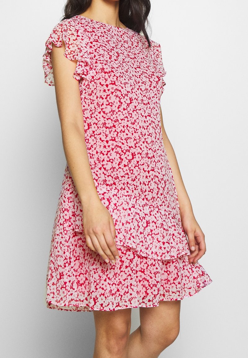 Blommig klänning i röd och rosa med korta volangärmar, lager på lager nertill, lättviktigt tyg och figurnära liv.