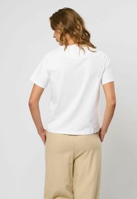 Witte katoenen t-shirt met korte mouwen en een ronde hals, gecombineerd met losse beige broeken. Achteraanzicht laat een ontspannen pasvorm zien.