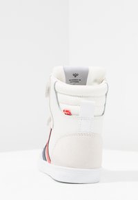 Höga sneakers med en krämvit ovandel med mockadetaljer, textilfoder, röda och navy randiga inslag samt en etikett som anger designens ursprung.