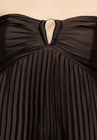 Μαύρο φόρεμα χωρίς λουριά με πιέτες και ασημένιο δαχτυλίδι στη μέση του μπούστου, που αναδεικνύει την υφή του υφάσματος και τις πτυχώσεις.