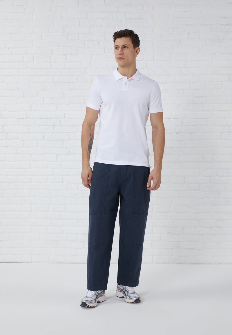 Witte polo shirt met korte mouwen en marineblauwe broeken met elastische taille, gecombineerd met zilveren sportschoenen. Gemaakt van soepele katoen en met een relaxte pasvorm.