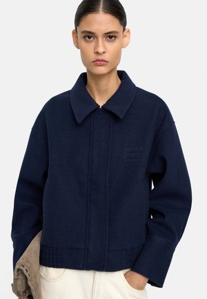Granatowa wełniana kurtka z szerokim kołnierzem, przednią kieszenią i haftowanymi detalami. Luźny krój z opadającymi ramionami i teksturowanym materiałem.
