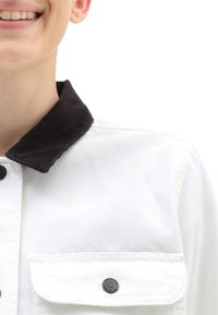 Veste en denim blanche avec col en velours côtelé noir, dotée de boutons-pression et d'une poche poitrine. Texture lisse avec un design structuré.