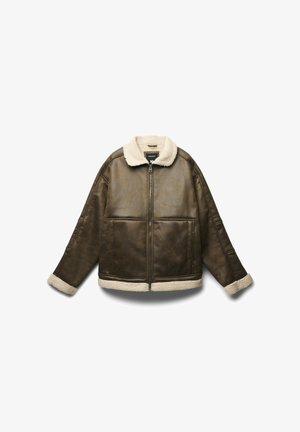 Brązowa kurtka z sztucznej skóry z kremowym kołnierzem i mankietami z owczej wełny; posiada zamek błyskawiczny z przodu oraz pudełkowy krój z widocznymi szwami.