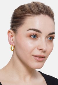 Boucle d'oreille en or, de forme circulaire, surface polie, épaisseur moyenne, portée à l'oreille gauche, complétant un top noir simple.