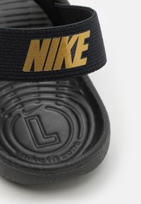 Černé klouzavé sandály s texturovanou gumovou podrážkou a látkovým páskem s zlatým logem Nike. Navrženy pro pohodlí a snadné nošení.