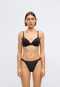 Schwarzer BH mit weicher Polsterung und verstellbaren Trägern, kombiniert mit einem transparenten schwarzen String mit gemustertem Bund.