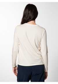 Lichtcrème lange mouw shirt met een ronde halslijn, zachte textuur en licht gebogen zoom, gecombineerd met donkere broeken.