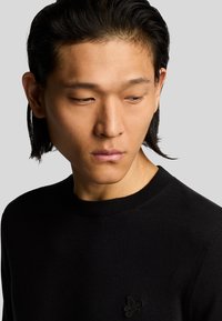 Maglione nero con collo rotondo, colletto a coste e tessuto testurizzato. Presenta un logo ricamato discreto sul petto.