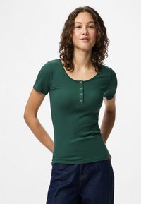 Top curto de mangas curtas verde com nervuras, decote redondo e quatro botões decorativos na frente, combinado com calções de ganga escuros.