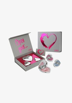 Sæt af hjerteformede kompakte spejle i sølvmetal med pink detaljer, præsenteret i en grå æske med et magenta hjerte design og pink indhold.