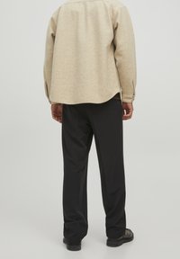 Beige wool shirt with long sleeves, rounded hem, and buttoned cuffs, paired with black straight-leg trousers and black shoes.