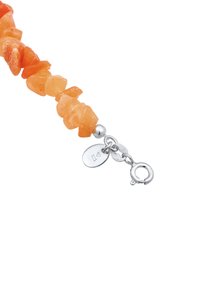 Armbander aus orangefarbenen Steinsplittern mit silberner Hardware, ausgestattet mit einem Karabinerverschluss und zwei kleinen Anhängern, die an der Kette befestigt sind.