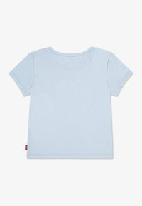 Lyseblå bomulls-T-skjorte med korte ermer og rund hals. Har en liten rød merkelapp nederst. Glatt tekstur.